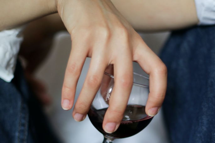 Das Bild zeigt die Hand einer jungen Frau, die ein Glas Rotwein hält.